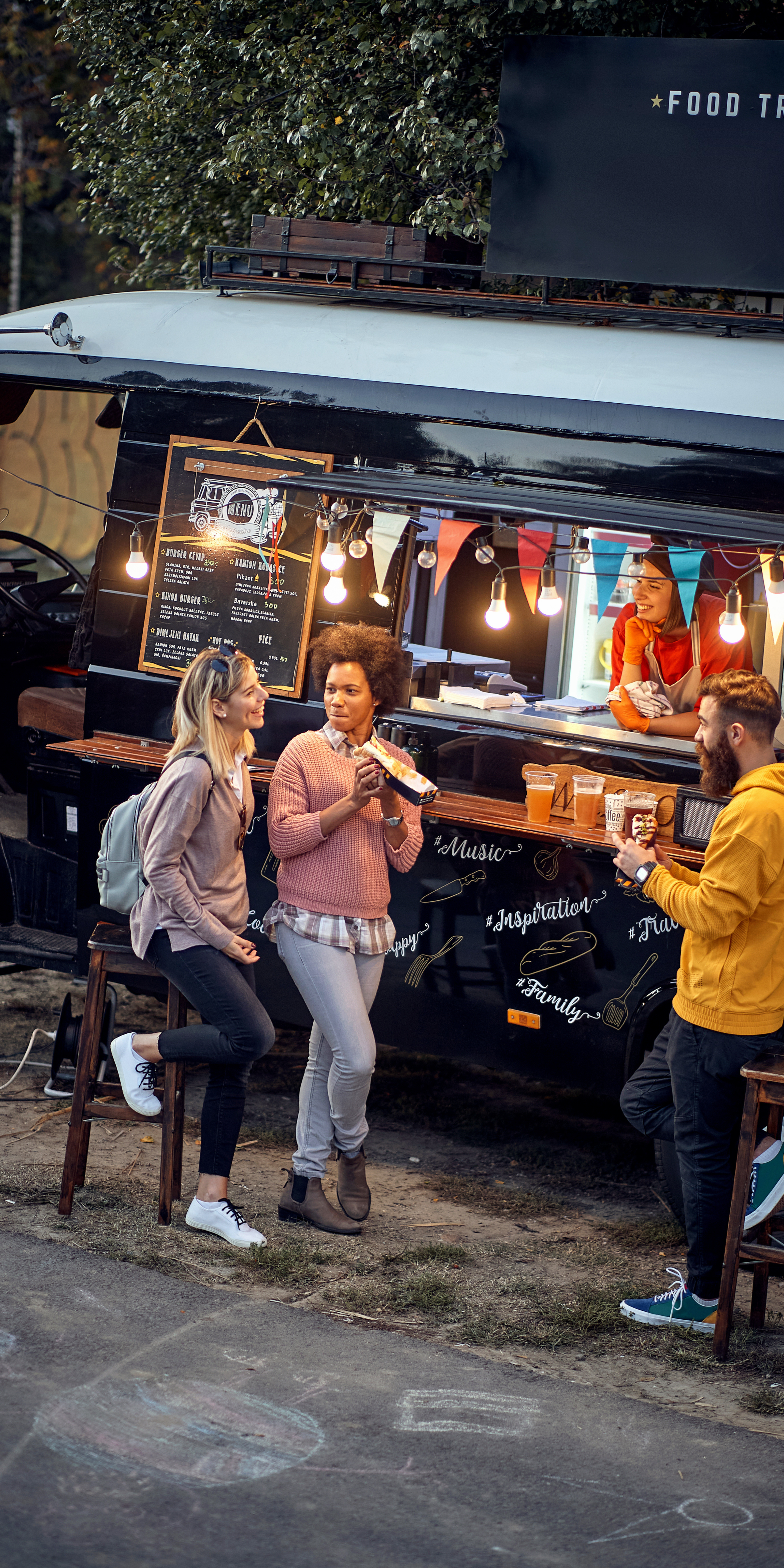 standard restaurant supply food truck supplies Food truck scene with three people enjoying food and drinks, showcasing a vibrant atmosphere, menu board, and string lights, relevant to the Food Truck Owners Expo promotion.